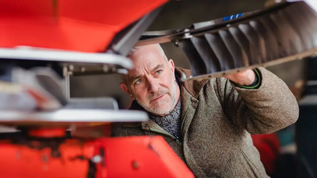 Landwirt kontrolliert aufmerksam das Streuaggregat eines Düngerstreuers.