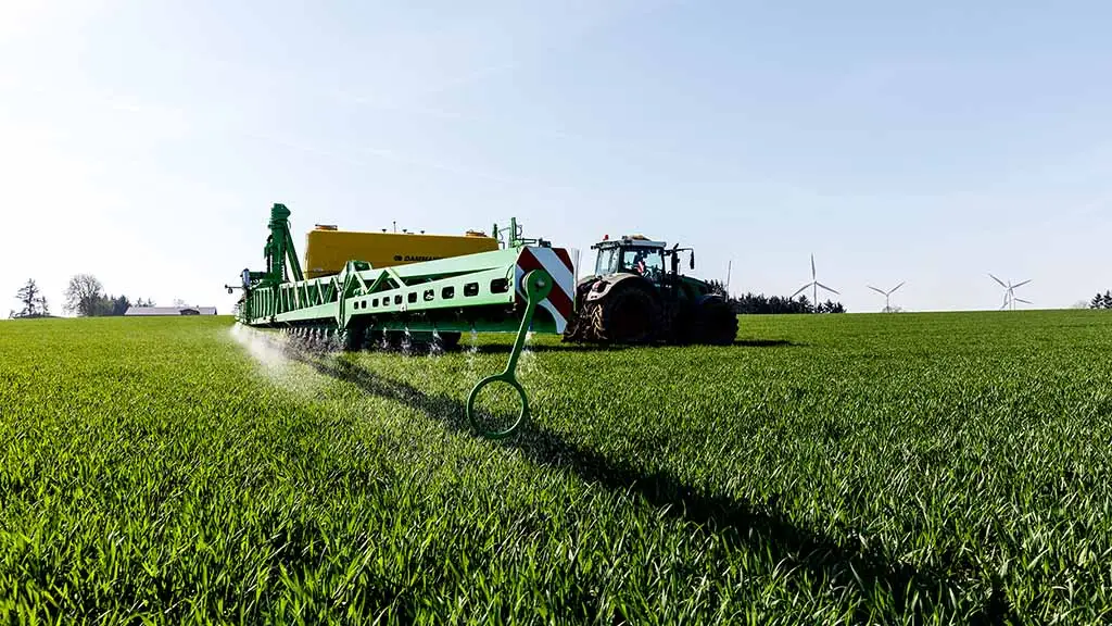 Traktor mit breiter Feldspritze bringt Flüssigdünger auf einem grünen Feld aus.