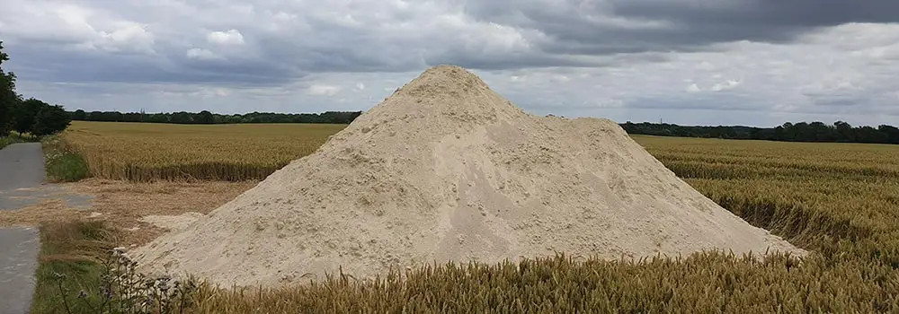 Großer Haufen Kalkaushub auf einem abgeernteten Feld unter bewölktem Himmel.