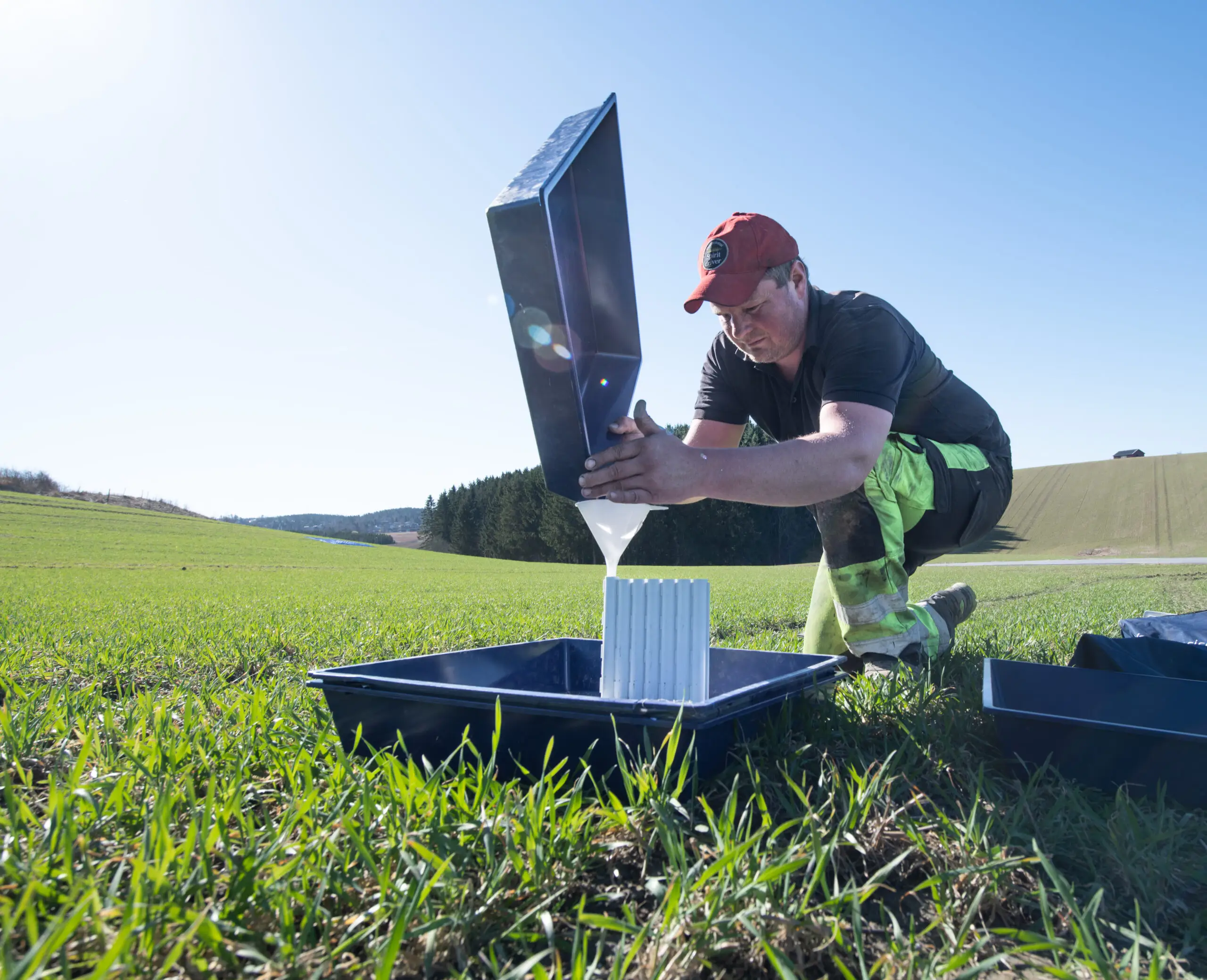 Landwirt kniet auf dem Feld und füllt aufgefangene Düngerpartikel aus Testschalen zur Kontrolle um.