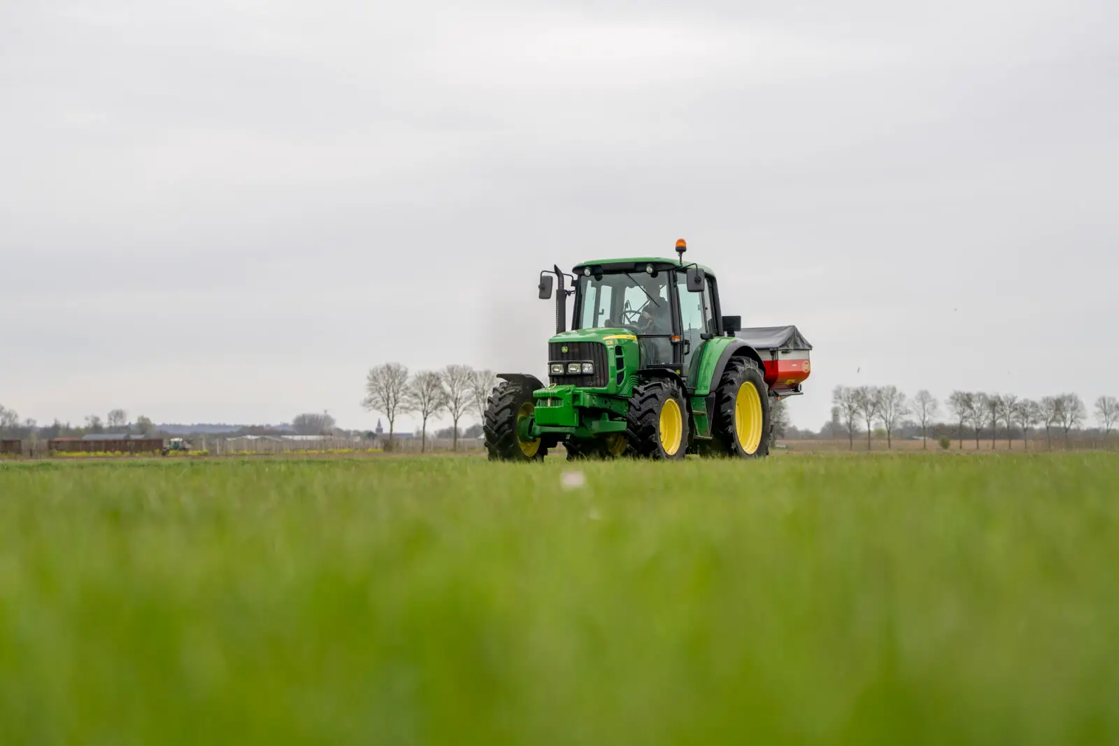 Traktor mit Anbau-Düngerstreuer bei der mineralischen Stickstoffdüngung im Frühjahr